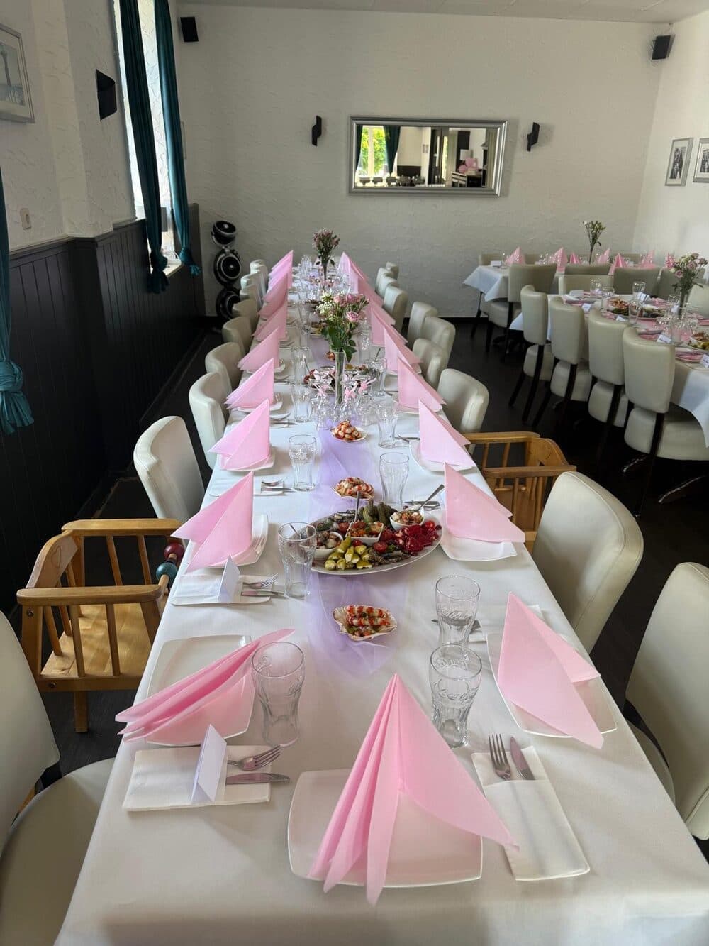 Festlich mit rosa Servietten, Blumen und Vorspeisenplatten gedeckte lange Tafel für eine Familienfeier in der Taverne Mykonos